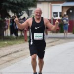 Joyful runner at a race finish line outdoors, raising arms in celebration.